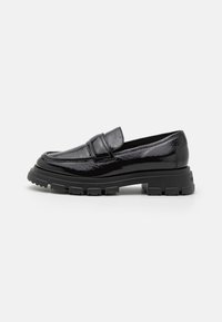 Zwarte gepatineerde leren instapper met een ronde neus, dikke rubberen zool en minimale stiksels. Heeft een kleine strap over de neus.