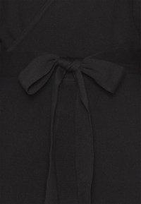 Tissu en maille noire avec un nœud noué centré à la taille d'un vêtement style portefeuille.