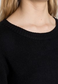 Svart tröja med en bred, ribbad halsringning och mjukt material, som framhäver en avslappnad passform med minimal detaljering.