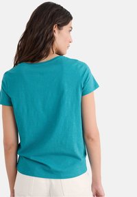 Krátký rukáv teal top vyrobený z měkké bavlny, s kulatým výstřihem a jednoduchým designem, se volným střihem a hladkou texturou.