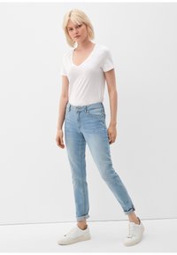 Jeans de color azul claro con corte ajustado, con una cintura de altura media, puños doblados y un detalle de costura en color marrón. Combinados con una camiseta blanca de cuello en V y zapatillas blancas.