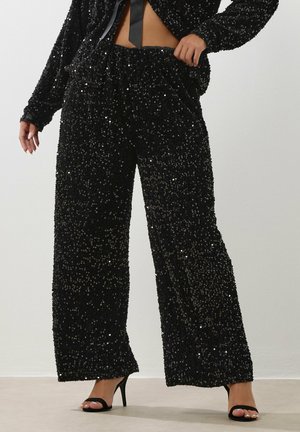 Zwarte met pailletten versierde wijde broek met een elastische tailleband en zachte textuur. Gecombineerd met zwarte hoge hakken sandalen.