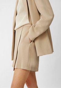 Lys beige skræddersyet jakkesæt med en blazer og matchende shorts. Det teksturerede stof og de rene linjer skaber et sammenhængende udseende.