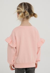 Jasnoróżowy sweatshirt z falbanami na rękawach, okrągłym dekoltem oraz ściągaczami przy mankietach i na dole. Miękka, strukturalna tkanina.