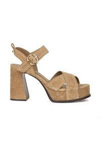 Sandalo con tacco a piattaforma in suede beige, con cinturini incrociati, chiusura con fibbia e tacco spesso per stabilità e altezza. Suola in gomma piatta.