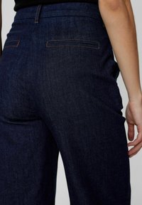 Blue denim pants featuring a high waist, side pockets, and a smooth texture, with contrasting stitching and back pocket detailing.