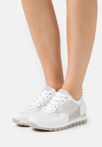 White sneakers with gray suede accents, mesh upper, round toe, and flat rubber sole; features lace-up closure and perforated design.