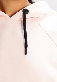 Felpa con cappuccio rosa chiaro, dotata di un laccio nero, caratterizzata da una superficie liscia e da un design minimalista.
