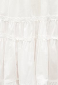 Tissu blanc avec plusieurs couches horizontales froncées, chaque couche bordée d'un délicat galon en dentelle.