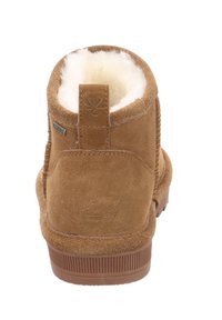 Braune Wildleder-Ankle-Boots mit einem weichen, weißen Fellfutter, einem Logodetail auf der Rückseite und einer strukturierten Gummisohle. Verfügt über einen kleinen Zugriemen für einfachen Einstieg.