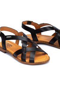 Zwarte leren sandalen met kruislings gemaakte banden, tan gekussioneerde zolen en een platte kurkzool. Verstelbare enkelband met een gouden gesp.