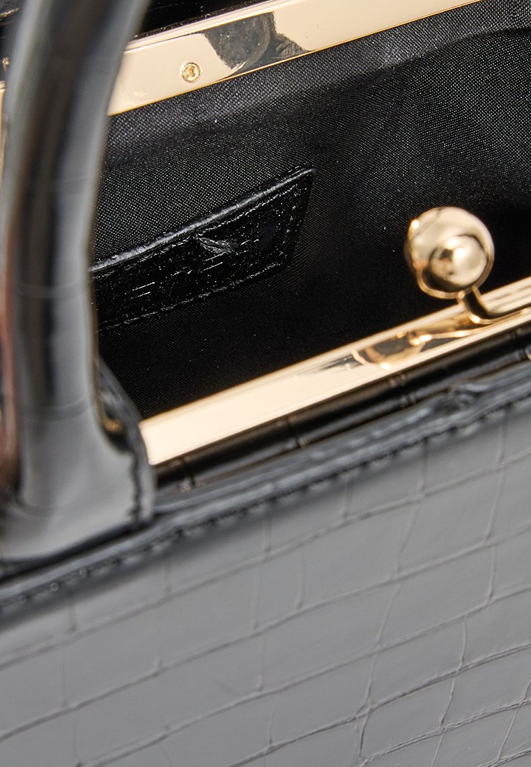 Intérieur d'un sac à main noir en croco embossé avec une texture lisse, quincaillerie dorée, doublure noire, et une petite poche avec une finition brillante.