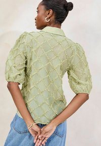 Hellgrüne, transparente Bluse mit Diamantmuster, Rüschendetails und Puffärmeln. Sie verfügt über einen klassischen Kragen und hat eine lockere Passform.