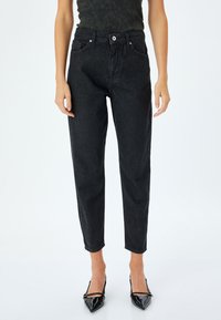 Svarta denimjeans med hög midja, smal benprofil, framfickor och detalj med knappstängning. Bärs med svarta spetsiga klackskor.