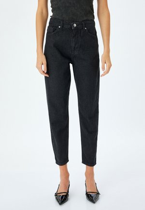 Jeans de denim negro con talle alto, pierna ajustada, bolsillos frontales y detalle de cierre con botón. Combinados con tacones negros de punta afilada.