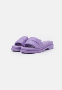 Lila slide-sandaler med överlappande remmar, tillverkade av mjukt material. Tjocka sulor med strukturerat mönster för grepp och stöd.