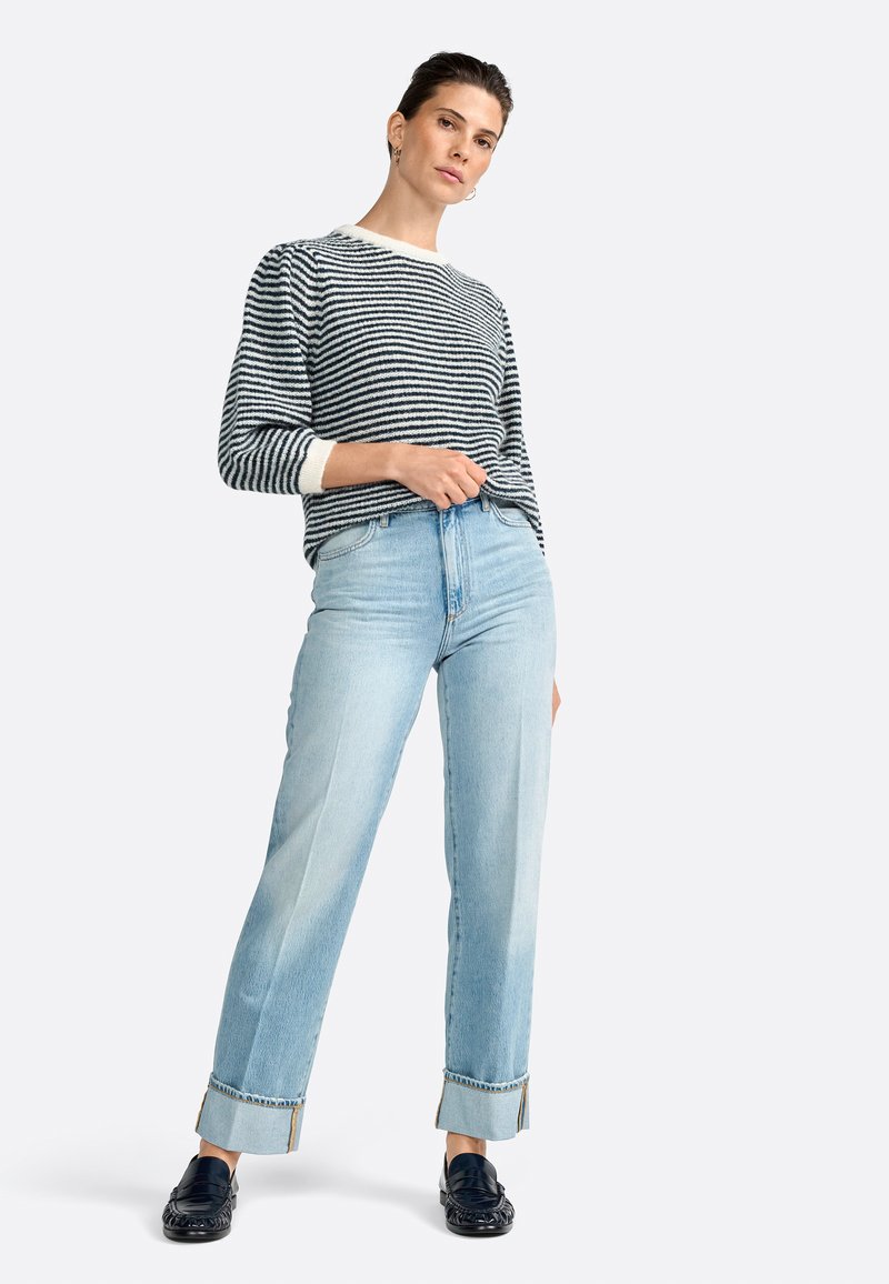 Striped knit sweater in navy and cream, paired with light blue straight-leg jeans featuring cuffed hems and black loafers.