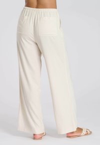Pantalons larges en créme légers avec une taille élastique, deux poches arrière et un tissu lisse, légèrement texturé.