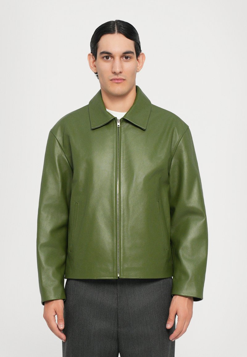 Chaqueta de cuero verde con cuello, cremallera frontal y bolsillos laterales. Presenta una textura suave y un ajuste cuadrado y relajado.