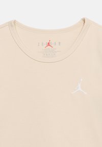 Μπεζ T-shirt Jordan με στρογγυλή λαιμόκοψη, με λευκό λογότυπο Jumpman κεντημένο στο στήθος και τυπωμένες πληροφορίες μεγέθους και φροντίδας στο εσωτερικό του γιακα.