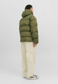 Chaqueta acolchada verde oliva con capucha, diseño acolchado y corte relajado. Combinada con pantalones holgados de color crema y zapatillas deportivas.
