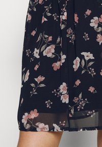 Vestido negro con un patrón floral que presenta flores en tonos rosa pálido y blanco. Tejido ligero con un diseño plisado y un dobladillo justo por encima de la rodilla.