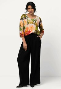 Blusa con motivo floreale in colori vivaci, abbinata a pantaloni neri a gamba larga. La blusa presenta una vestibilità morbida e maniche a tre quarti.