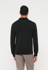 Mustast kootud kampsun sallikaelusega ja soonikkoes varrukasäärtega. Sirge lõige, sileda tekstuuriga, kantud helehallide pükstega.