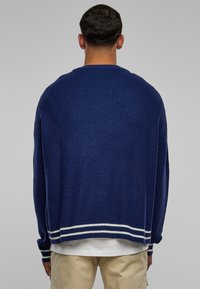 Marineblauwe gebreide trui met een losse pasvorm, geribbelde structuur en witte gestreepte accenten bij de zoom en manchetten.