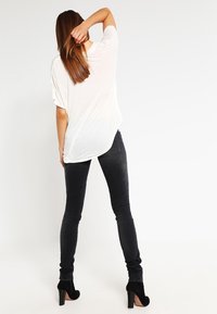White, loose-fitting T-shirt with short sleeves paired with fitted black skinny jeans. The outfit is completed with black high-heeled shoes.