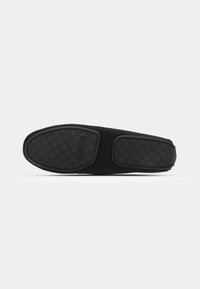 Chaussure noire à enfiler avec une semelle en caoutchouc texturé présentant un motif en losanges. Le matériau supérieur est lisse et ne présente pas de fermetures visibles.