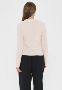 Light pink sweater with long sleeves, round neckline, soft texture, fitted waist, and ribbed cuffs. Worn with black loose-fitting pants.