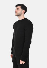 Maglione nero a maniche lunghe realizzato in tessuto a coste. Presenta un collo rotondo e polsini aderenti, con una silhouette dritta.