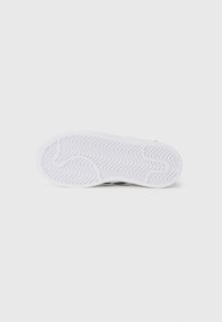 Sapatilha branca com sola de borracha texturizada, apresentando padrão de espinha de peixe para aderência e bordas suaves. Design minimalista, predominantemente monocromático.