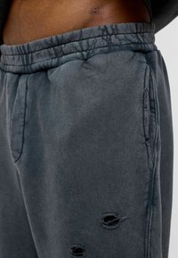 Donkergrijze joggingsbroek met een zachte textuur, voorzien van een iets elastische tailleband, zijzakken en versleten details dicht bij de zoom.