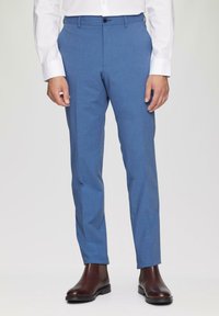 Blaue maßgeschneiderte Hose aus glattem Material, schlanke Passform und mit einem Knopfverschluss, kombiniert mit braunen Chelsea-Stiefeln.