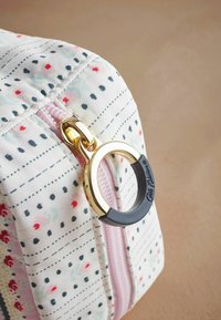 Klein rechthoekig tasje van stof met een bloemenpatroon, een roze rits, gouden hardware en een zwarte rubberen accent op de ritsgrijper.