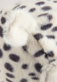Umělá kožešina s krémovým základem a černými skvrnami, s měkkým chomáčkovým detailem. Textura je nadýchaná a mírně lesklá.