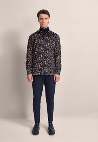 Hemd mit Marine-Muster und floralem Design, lange Ärmel und Knopfverschluss, kombiniert mit schmalen dunklen Hosen und schwarzen Schuhen.