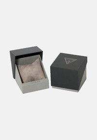 Twee kleurige grijze Guess-juwelenboxen, waarvan één open met een grijze suede kussen binnenin en de ander gesloten met het logo op de bovenkant.