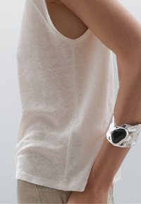 Lys beige, ærmeløs top lavet af blødt stof med en afslappet pasform. Begge dele ledsages af et skinnende sølvmanchetarmbånd med en sort detalje.