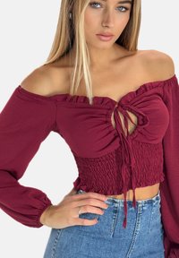Bordeaux off-shoulder top med flæse detajer, frontbinding og smocket talje; lange ærmer og blød stoftekstur.