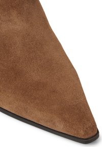 Zapato de ante marrón con puntera afilada y textura suave, con una suela negra. El diseño es elegante con una parte delantera afilada para un aspecto refinado.