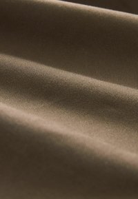 Tekstūru audums siltā brūnā nokrāsā, ar gludām viļņiem un smalku ribojumu, uzsverot tā maigo un aicinošo izskatu.