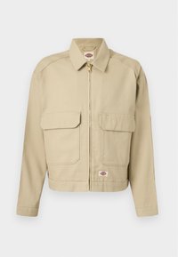 Μπεζ ζακέτα με φερμουάρ, δύο μεγάλες εμπρόσθιες τσέπες με καπάκι, ευθεία γιακά, μακριά μανίκια και ετικέτα της μάρκας Dickies στο στήθος και στο τελείωμα.