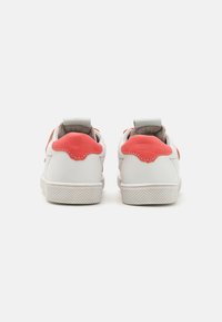 Zapatillas blancas con acentos de cuero coral en el talón, detalle curvado en la parte posterior, suela de goma texturizada y tira de agarre para facilitar su uso.