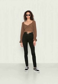 Top cropped com padrão de onça marrom, com mangas longas e bufantes, combinado com jeans skinnys pretos e sapatilhas pretas, completando o visual casual.