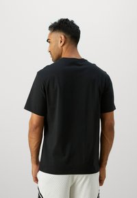 Sort bomulds t-shirt med korte ærmer og rund halsudskæring, vist fra ryggen. Glat tekstur og enkel design.