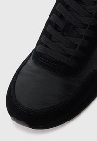 Zwart sneaker met een mix van glad nylon en gestructureerd suede, met platte veters en delicate stiksels langs de bovenzijde.