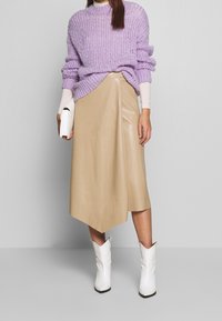 Knittat lavendelfärgade tröja, krämfärgad undertröja, beige fusk läderomslag kjol med sned fåll och vita western-inspirerade ankelstövlar.